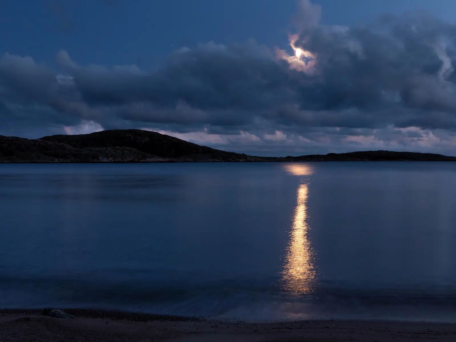 A blue night horizon with moonlight reflecting on calm water.