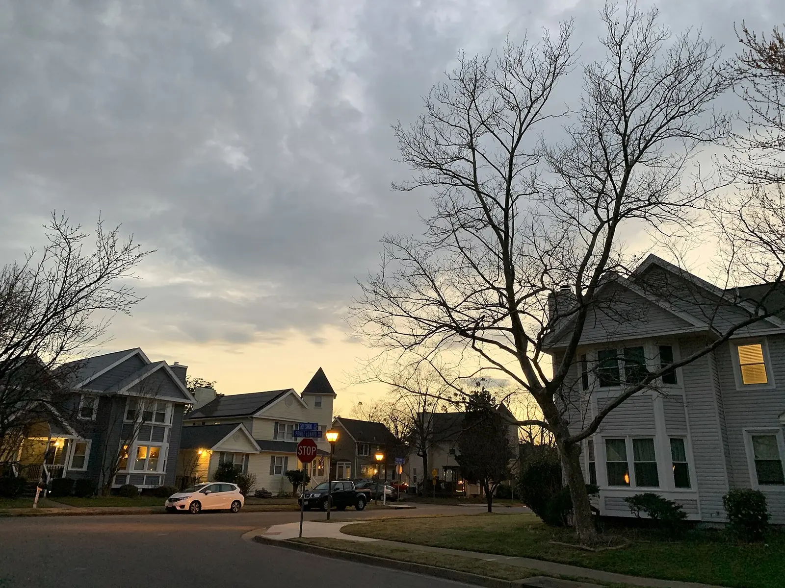 A quiet residential street at dusk with house lights beginning to glow.