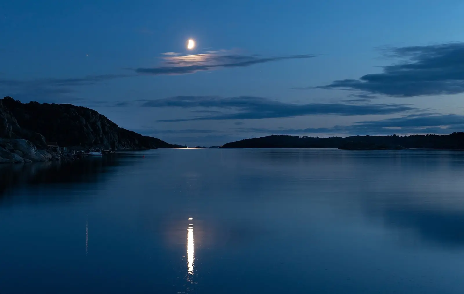 Moonlight reflected in still water with dark islands at dusk.