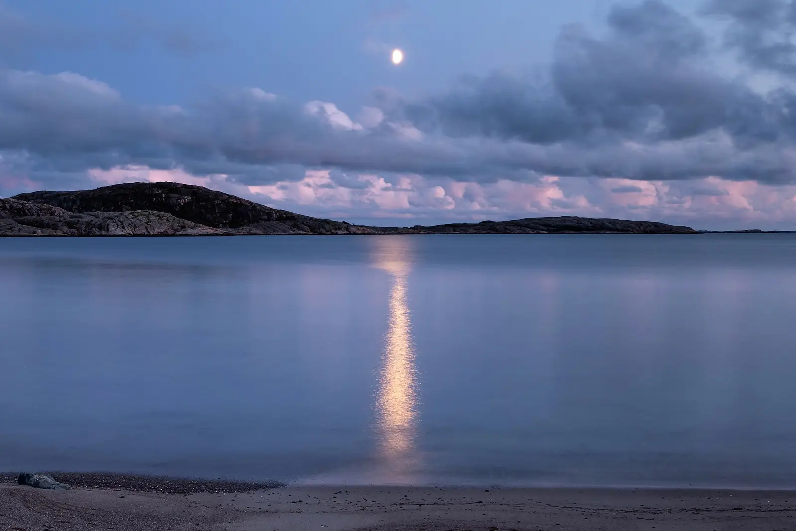 Moonlight reflected over still dark water beneath a clouded night sky.
